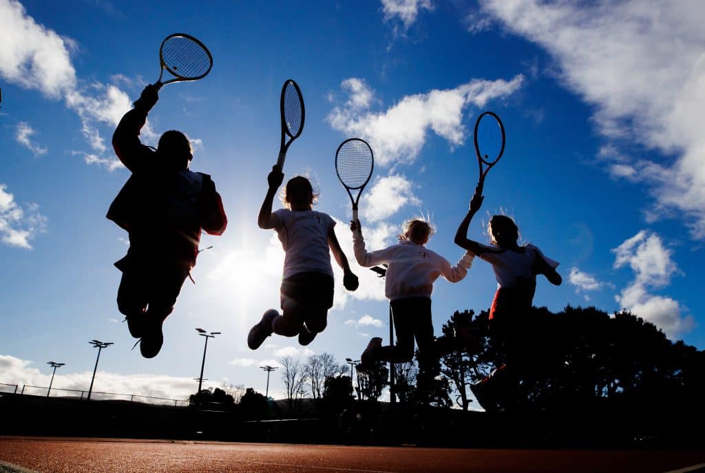 Kids jumping with tennis rackets in hands on a sunny day