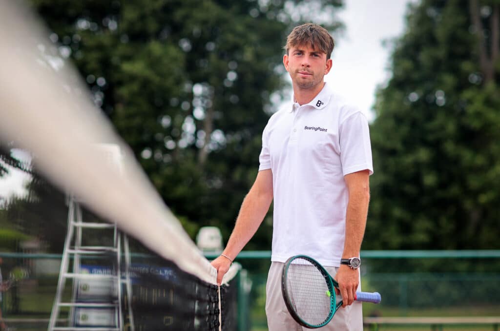 Male tennis player wearing white holding a racket and standing beside a net